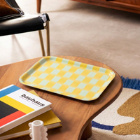 Plateau jaune et bleu clair à motif damier Wrap Magazine, posé sur une table basse en bois.